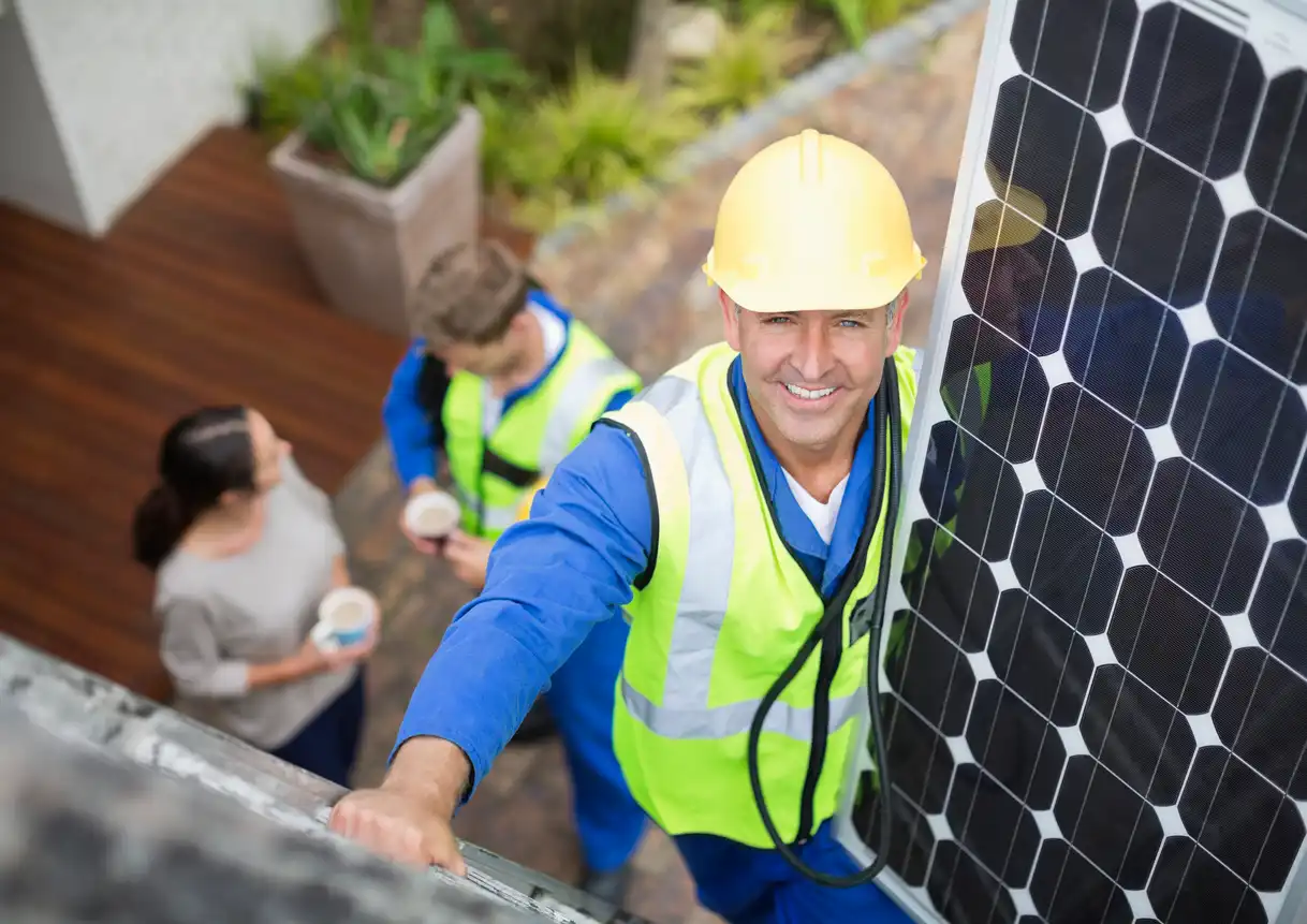Engenheiro instalando painéis solares em telhado, com equipe de trabalhadores ao fundo, promovendo energia renovável e sustentabilidade.