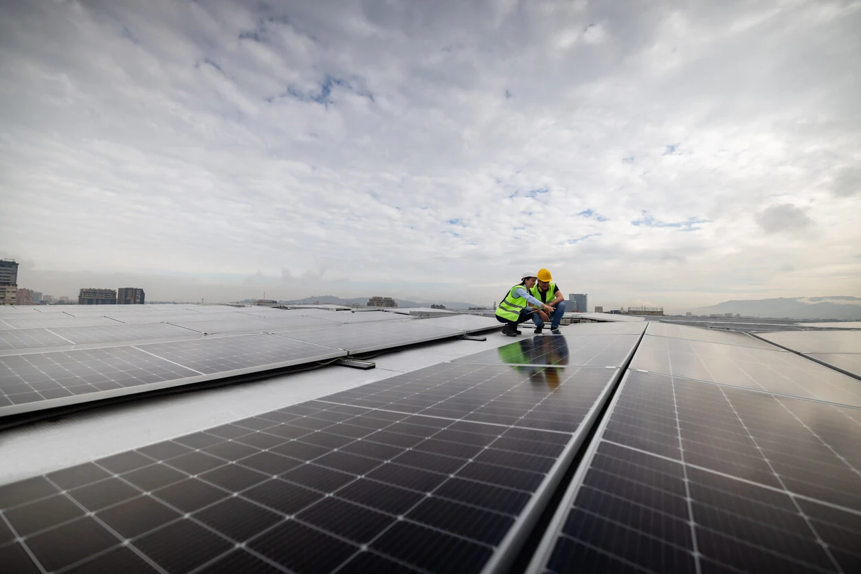Engenheiros instalando painéis solares em um telhado com céu nublado ao fundo, promovendo energia renovável e sustentabilidade.