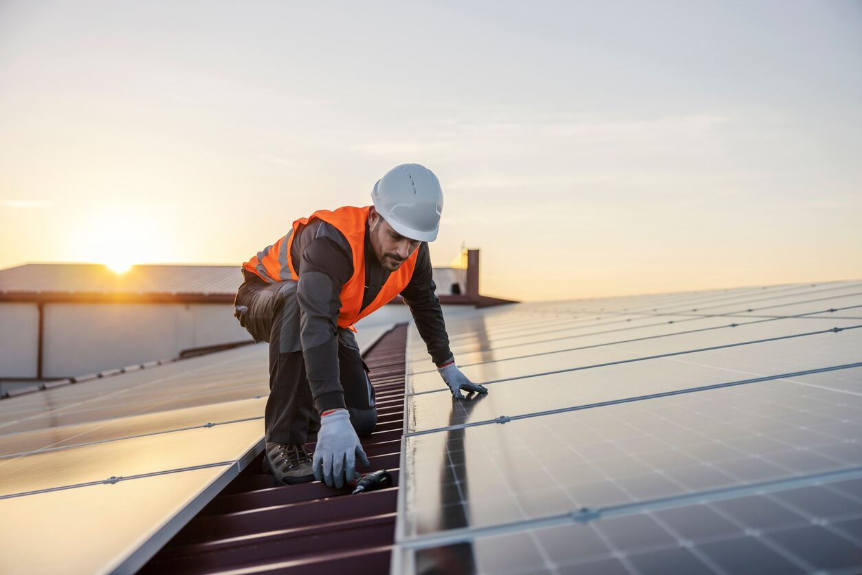 Técnico instalando painéis solares em um telhado ao pôr do sol, representando a implementação de sistemas fotovoltaicos em residências. Imagem ideal para ilustrar a análise de quantas placas solares são necessárias para atender ao consumo energético doméstico.