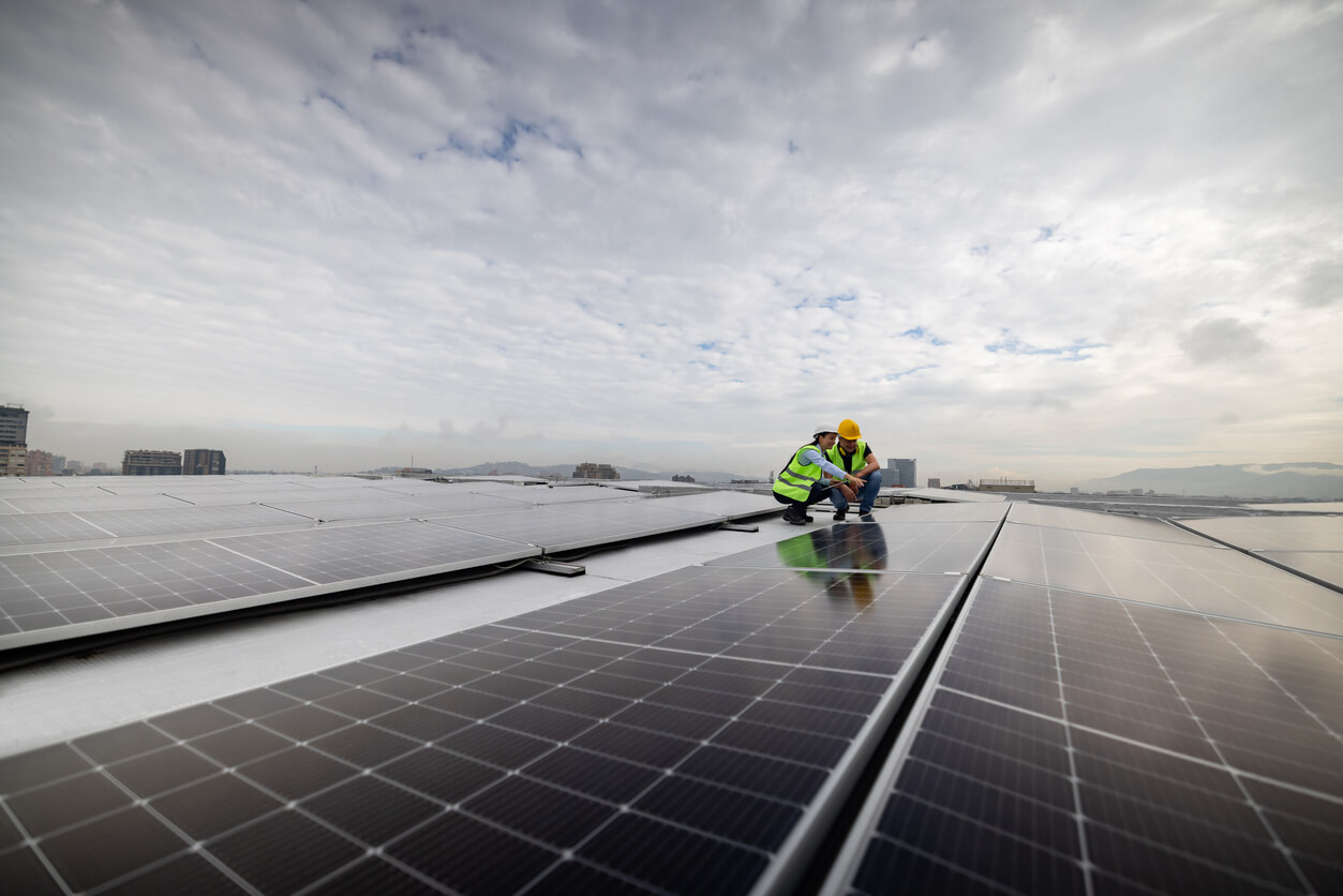 Dois profissionais analisando painéis solares em um grande telhado urbano, simbolizando o uso de financiamentos para projetos de energia solar. Imagem ideal para abordar a taxa de financiamento de energia solar, destacando acessibilidade e benefícios econômicos.