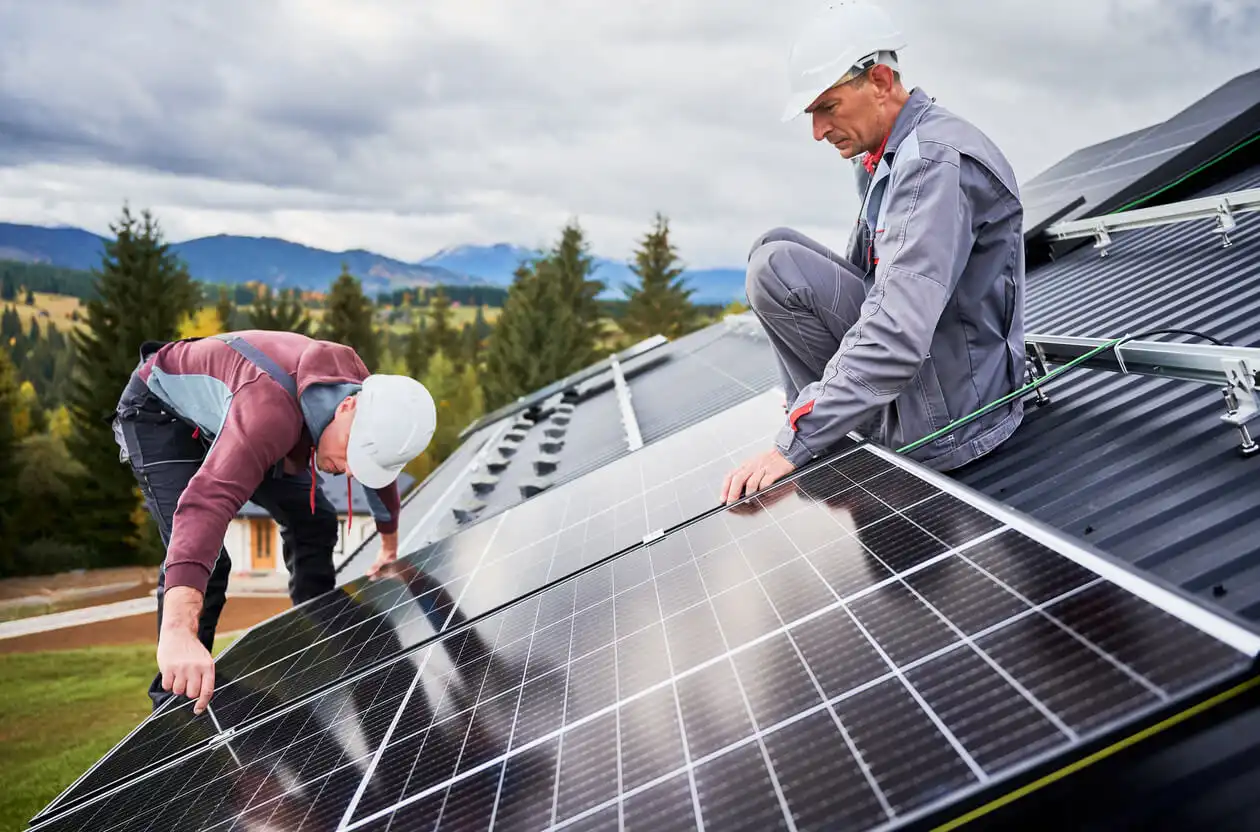 Homens instalando painéis solares em telhado resistente ao vento, simbolizando energia renovável e sustentabilidade.