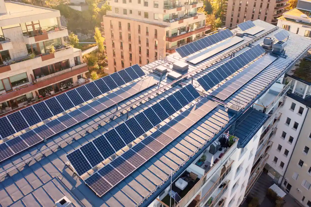 Painel solar no telhado de um prédio residencial moderno em uma área urbana, aproveitando energia renovável solar, com outros edifícios ao fundo.