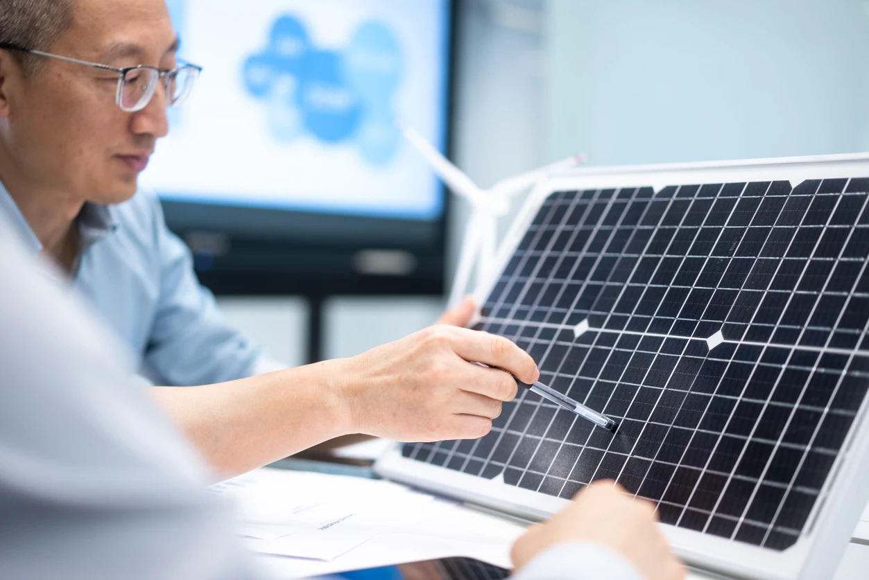 Um engenheiro observa e discute um painel solar durante uma reunião, destacando a importância da energia solar para o futuro sustentável.