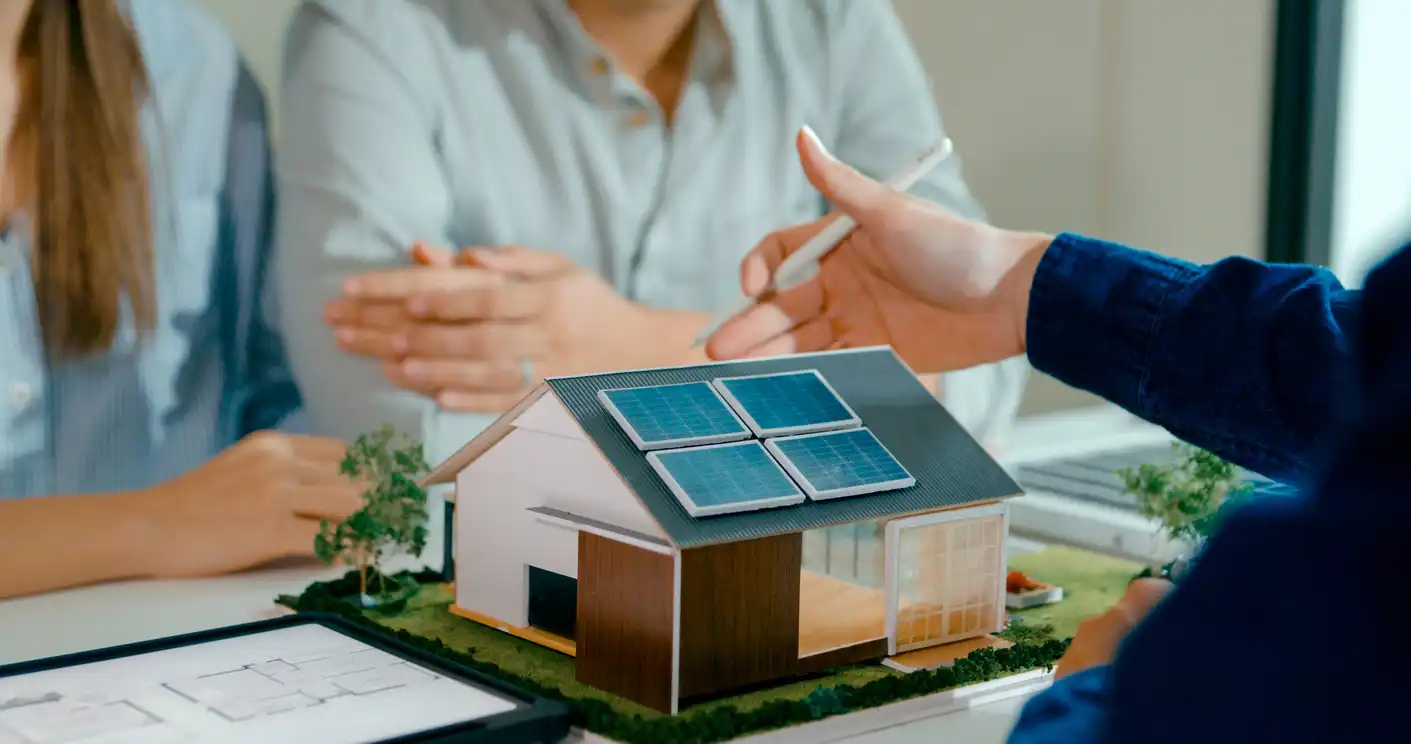 Reunião de profissionais analisando modelo de casa sustentável com painéis solares para energia renovável