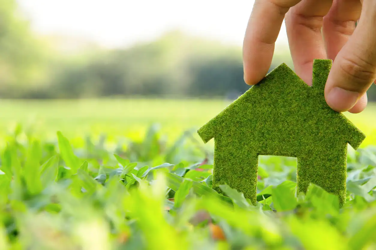 Mão segurando uma miniatura de casa feita de material semelhante a grama, simbolizando sustentabilidade e ecoeficiência na construção civil.