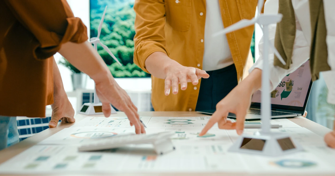 Equipe de profissionais analisando projetos de energias renováveis e energia solar em uma mesa de trabalho com modelos e documentos.