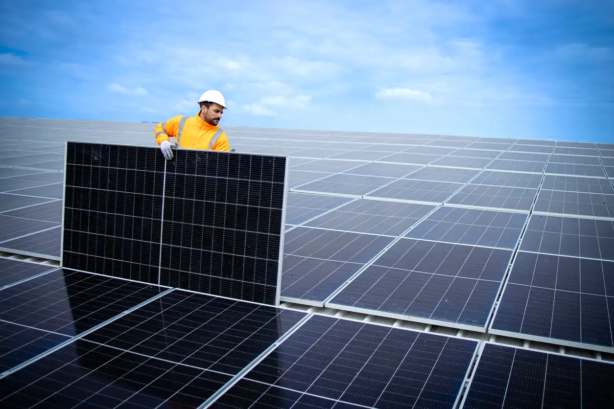 Engenheiro instalando painéis solares em usina de energia solar fotovoltaica ao ar livre, simbolizando energia renovável e sustentabilidade.