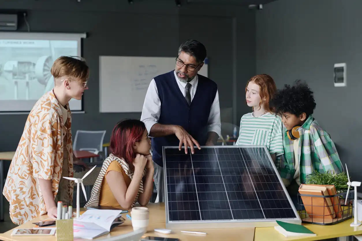 Imagem de um professor ensinando um grupo de crianças sobre energia solar, com painel solar em uma sala de aula moderna, promovendo sustentabilidade e educação ambiental.