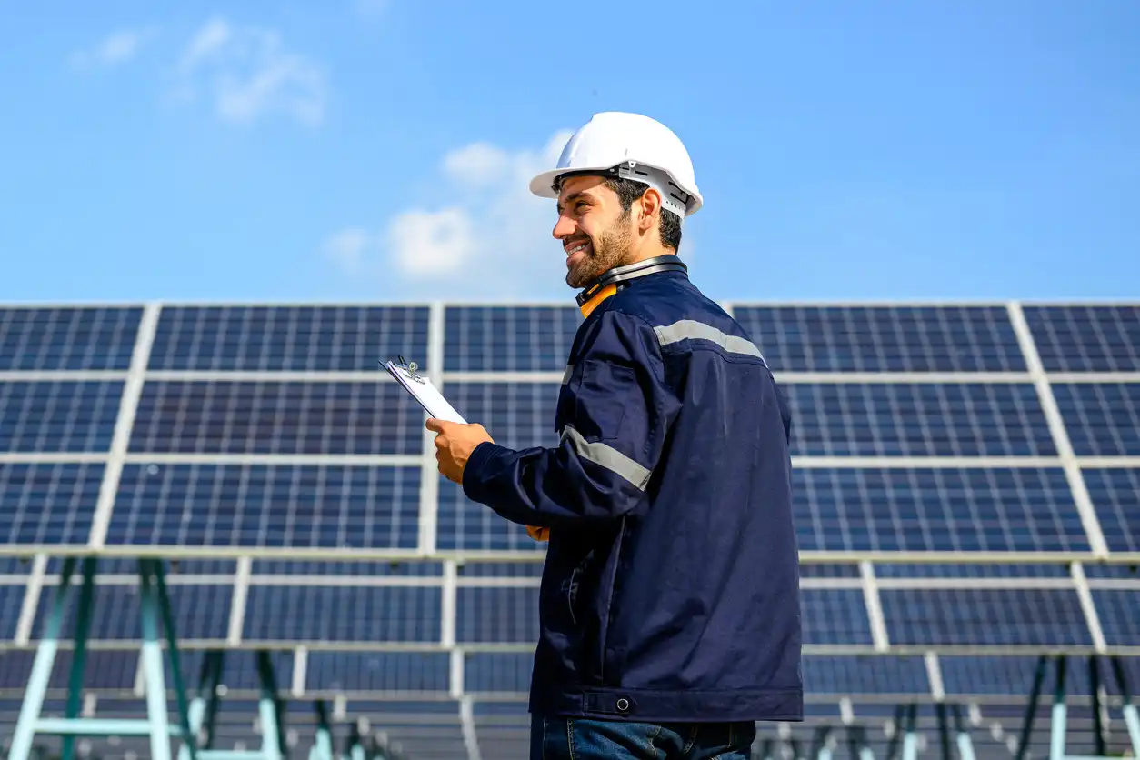 Engenheiro de energia solar analisando painéis solares em usina fotovoltaica ao ar livre, com céu azul ao fundo.