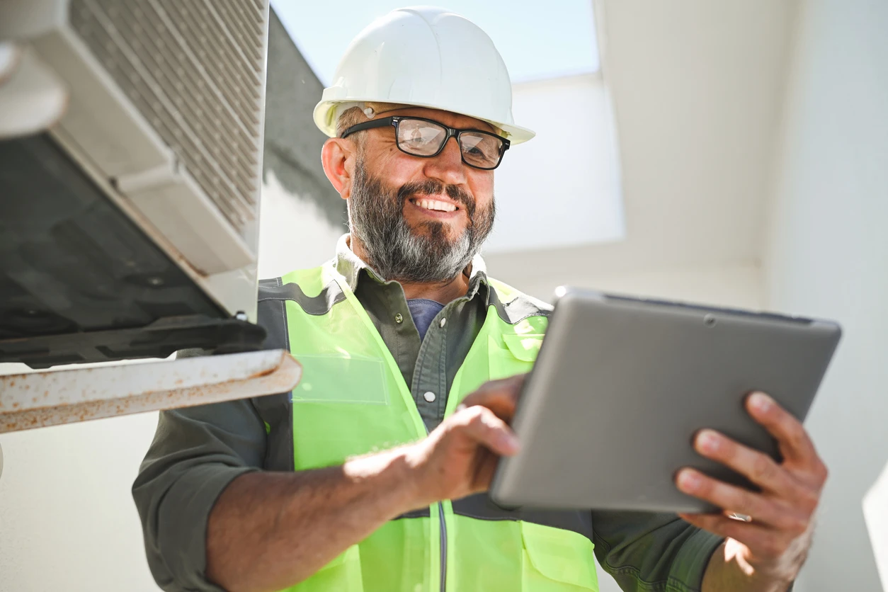 Engenheiro usando tablet em ambiente industrial, vestindo capacete de segurança e colete refletivo, verificando informações técnicas.