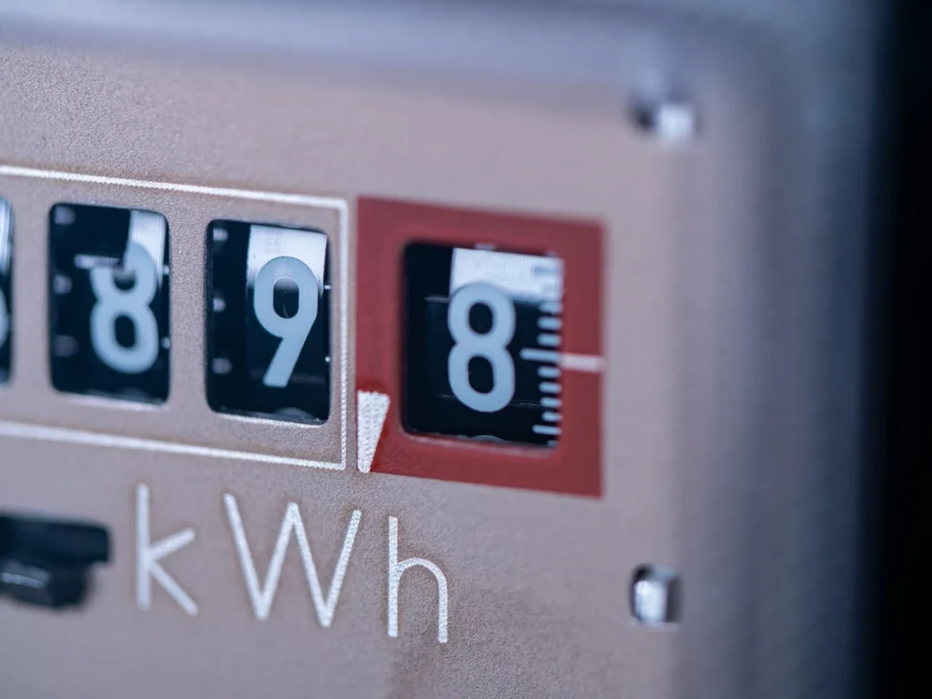 Imagem de um medidor de energia elétrica mostrando consumo de 8 kWh, com foco na leitura e detalhes do painel em fundo desfocado.