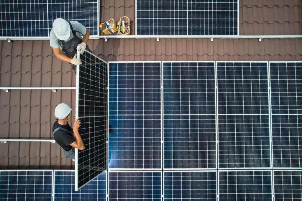 Dois trabalhadores instalando painéis solares em telhado com telhas de cerâmica, contribuindo para energia sustentável e uso de energia solar.