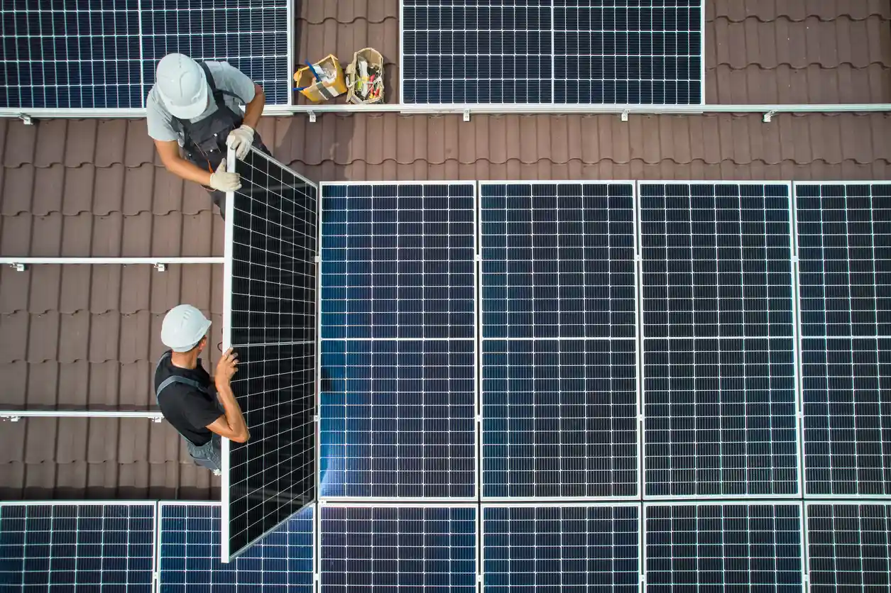 Dois trabalhadores instalando painéis solares em telhado com telhas de cerâmica, contribuindo para energia sustentável e uso de energia solar.