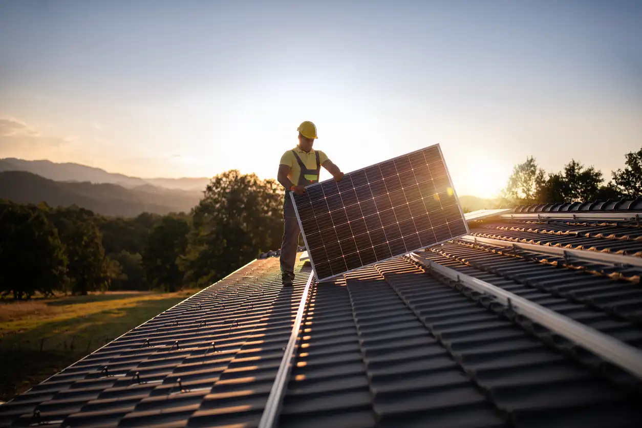 Profissional instalando painel solar no telhado com vista para o nascer do sol, promovendo energia sustentável e renovável.
