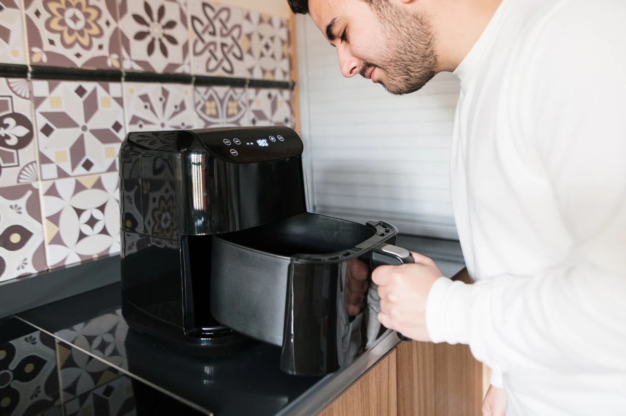 Homem preparando comida com uma air fryer moderna na cozinha