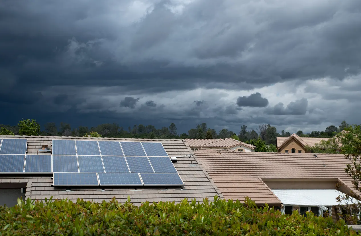 Telhados residenciais com painéis solares fotovoltaicos instalados, céu nublado e clima instável ao fundo, em uma cena de energia limpa
